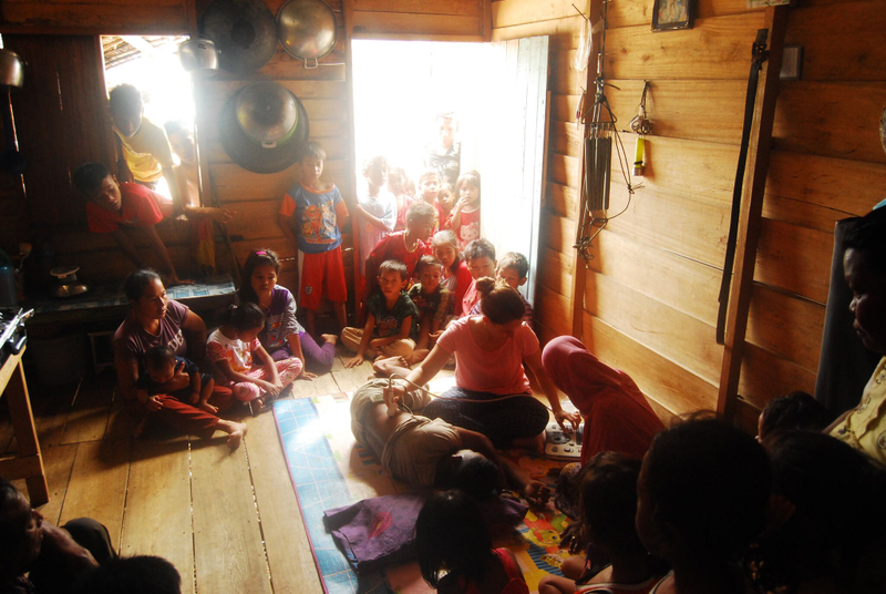 Villagers and curious children look on as researcher Melissa Ilardo takes spleen measurements using a portable ultrasound in a Bajau home.